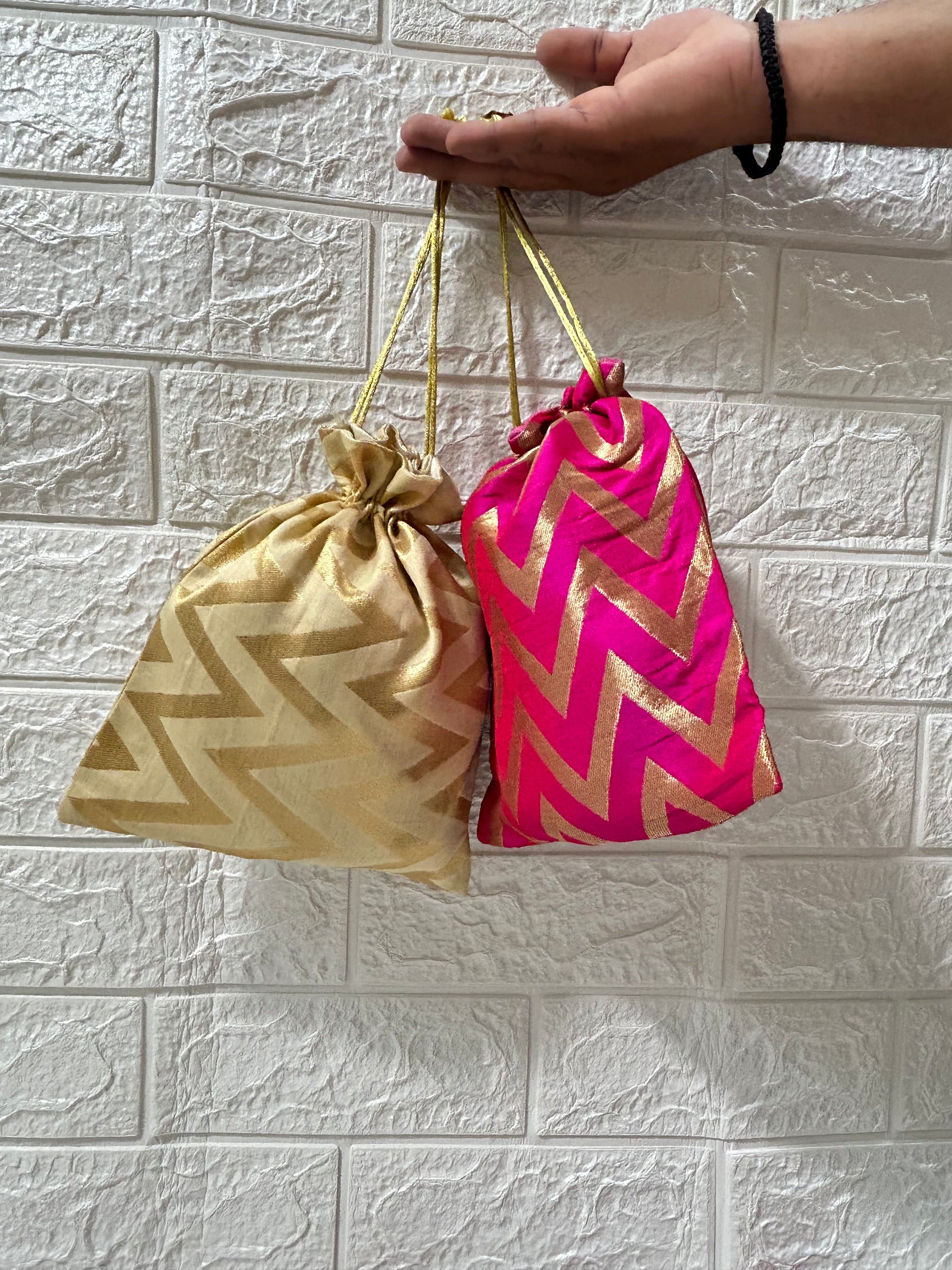 Hand holding two colorful Brocade Potli Bags in gold and pink with zigzag patterns