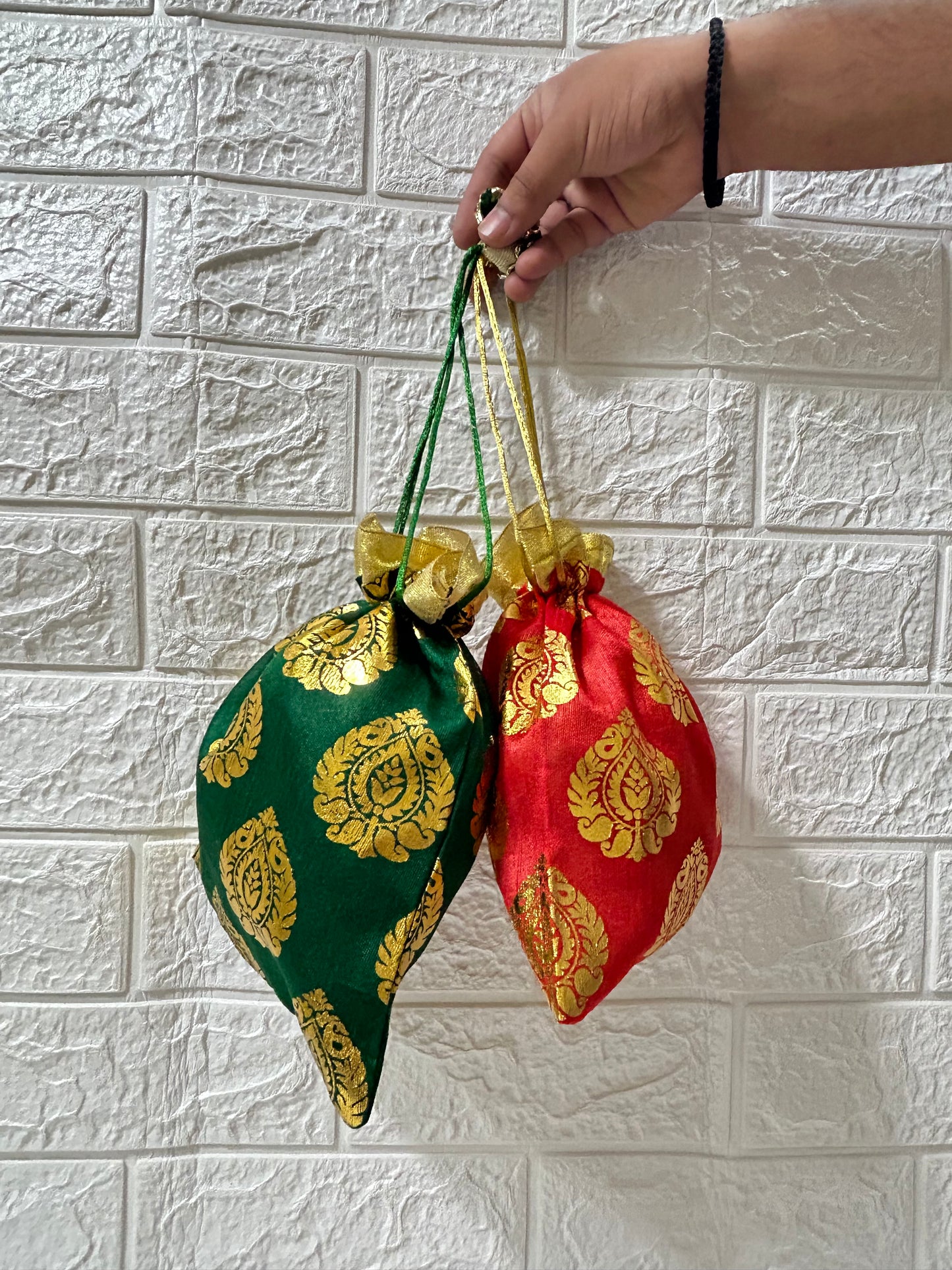 Hand holding green and red DesiTohfa gift packing potli bags with golden floral patterns