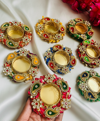 Decorative Diwali oil lamps with colorful embellishments on a white fabric background.