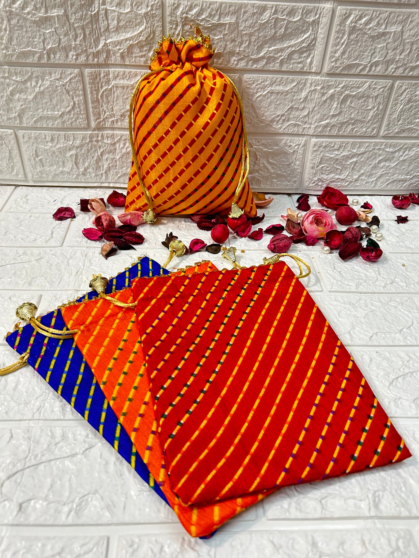 DesiTohfa multicolor Leheriya gift bags in orange, red, and blue with gold drawstrings and decorative dried flowers