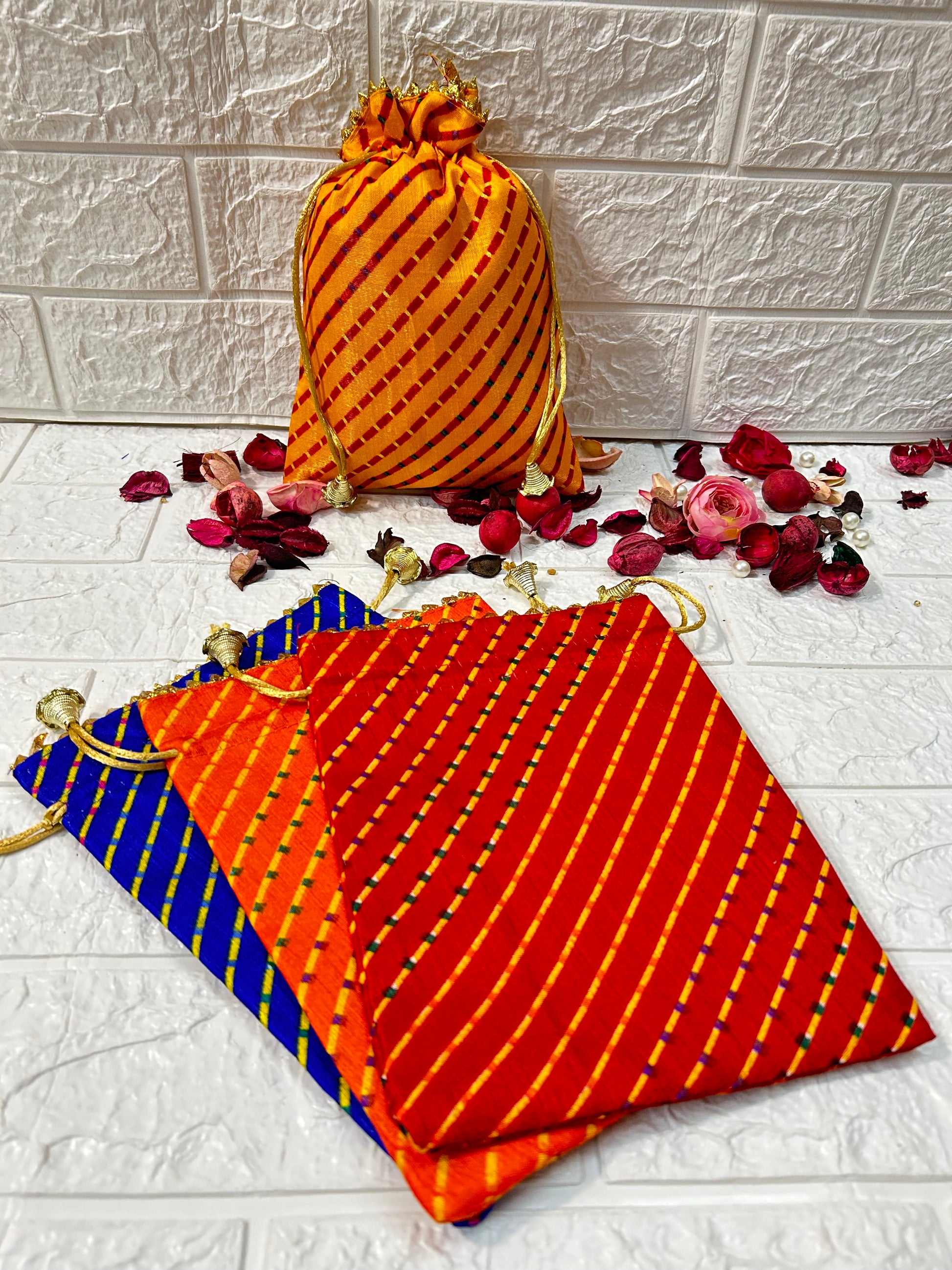 DesiTohfa multicolor Leheriya gift bags in orange, red, and blue with gold drawstrings and decorative dried flowers